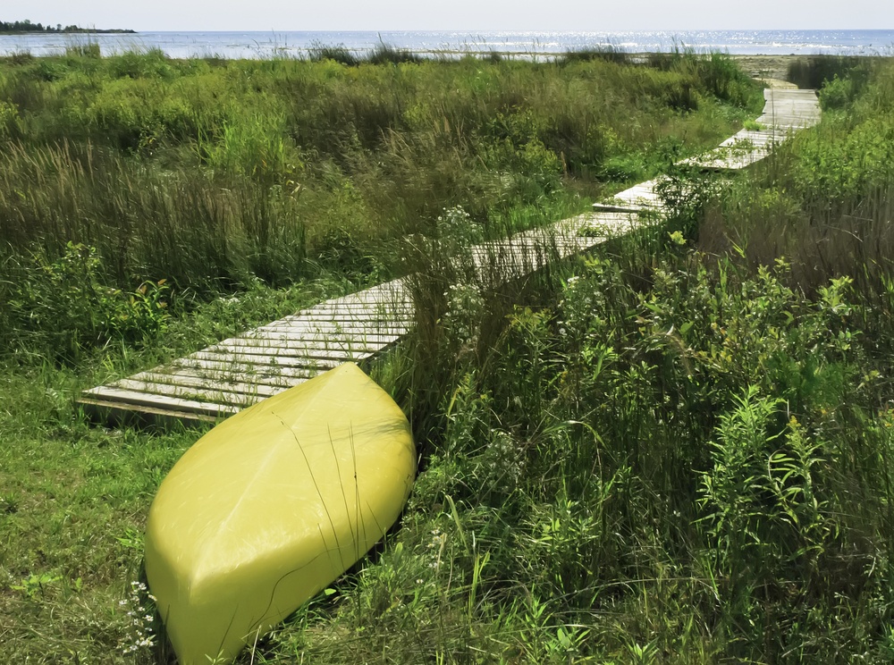 Yellow kayak, upside down, at end of boardwalk to beach